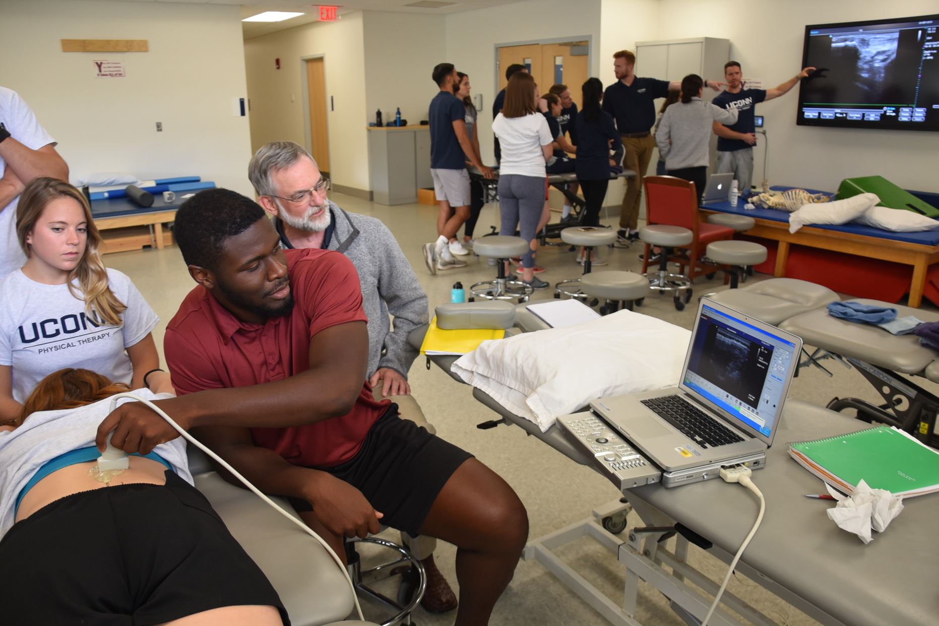 student practices an ultrasound on a classmate while faculty provide guidance
